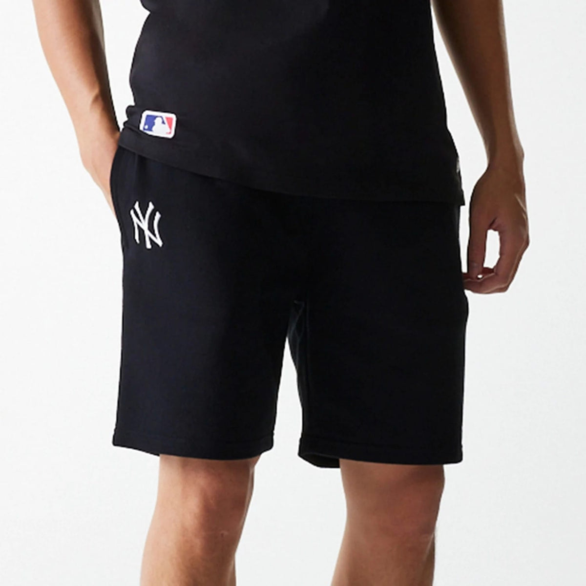 New Era New York Yankees MLB League Essential French Terry Black Shorts, front view showing the black shorts with a white embroidered New York Yankees logo on the left leg and part of a person’s hand resting against the right side.