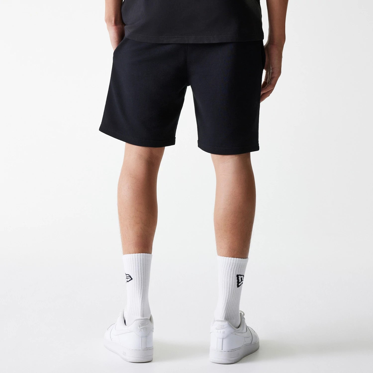 New Era New York Yankees MLB League Essential French Terry Black Shorts, rear view showing the plain black fabric ending above the knee with white socks featuring an embroidered New Era logo and white trainers below.