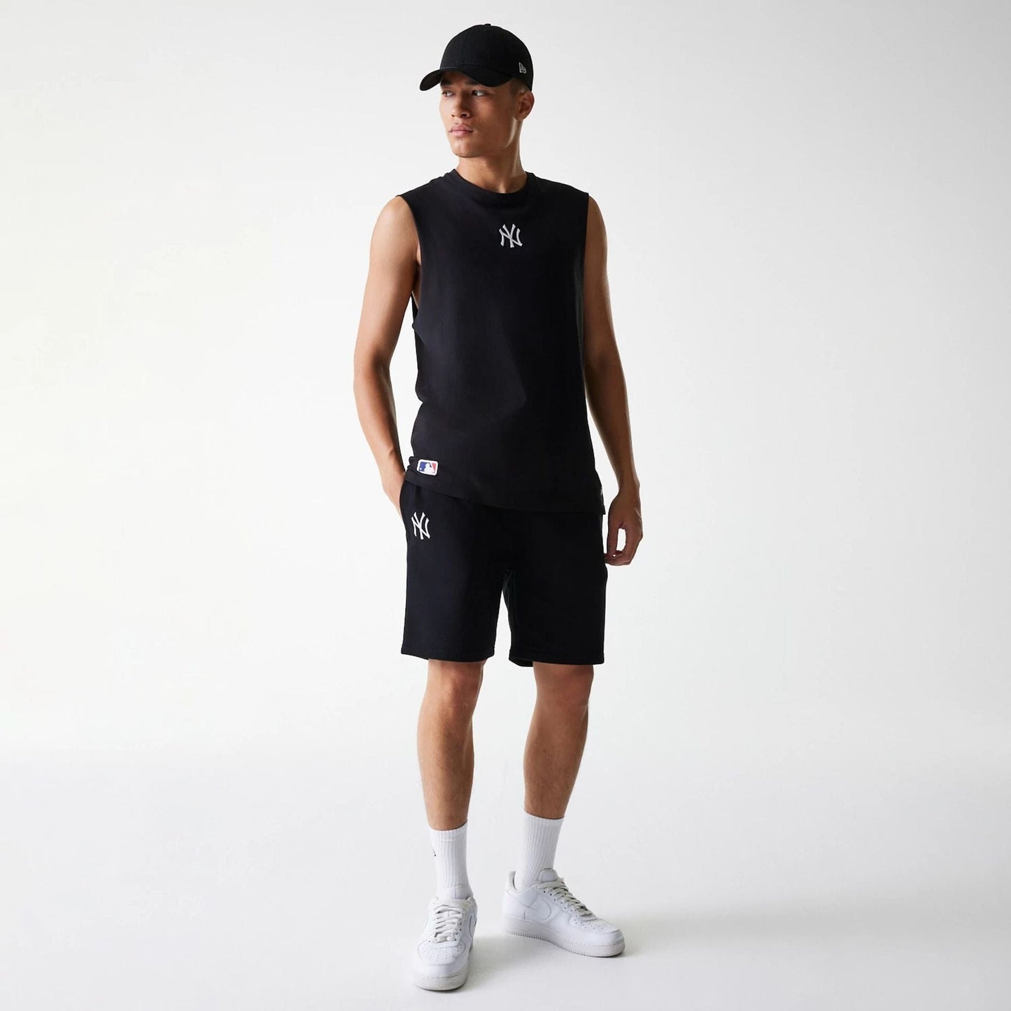 New Era New York Yankees MLB League Essential French Terry Black Shorts, on-model view showing the black shorts with a white embroidered Yankees logo on the left thigh, paired with a matching sleeveless top and a black cap.