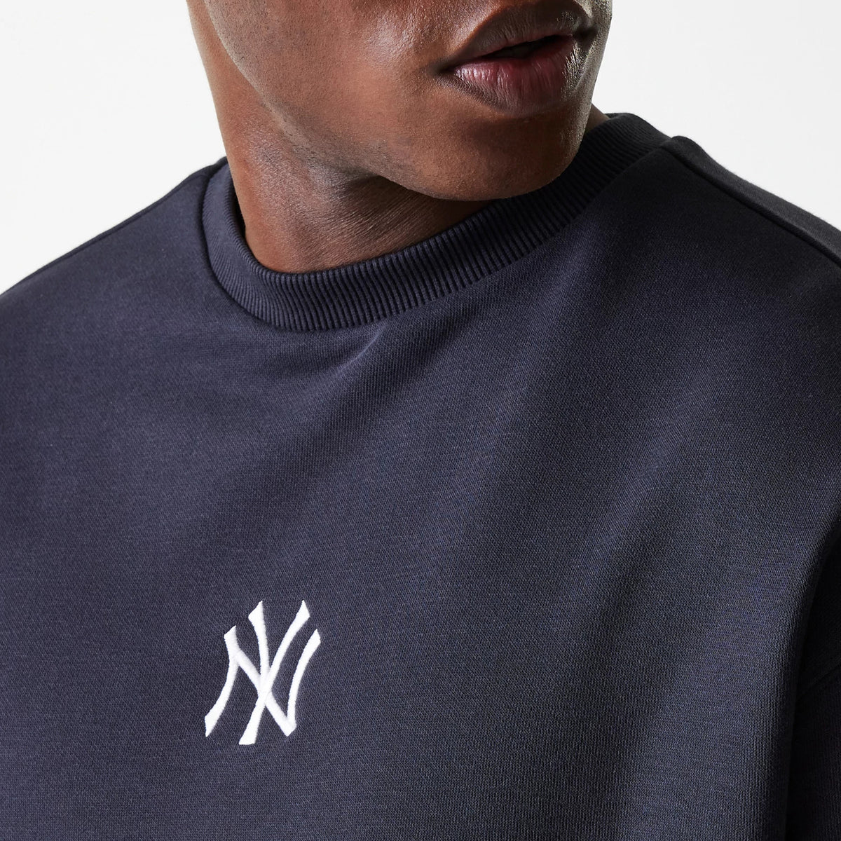 New Era New York Yankees MLB League Essential French Terry Navy Crew Neck Sweater, close-up view on a model showing the white embroidered NY logo on the left chest and ribbed crew neck detail.