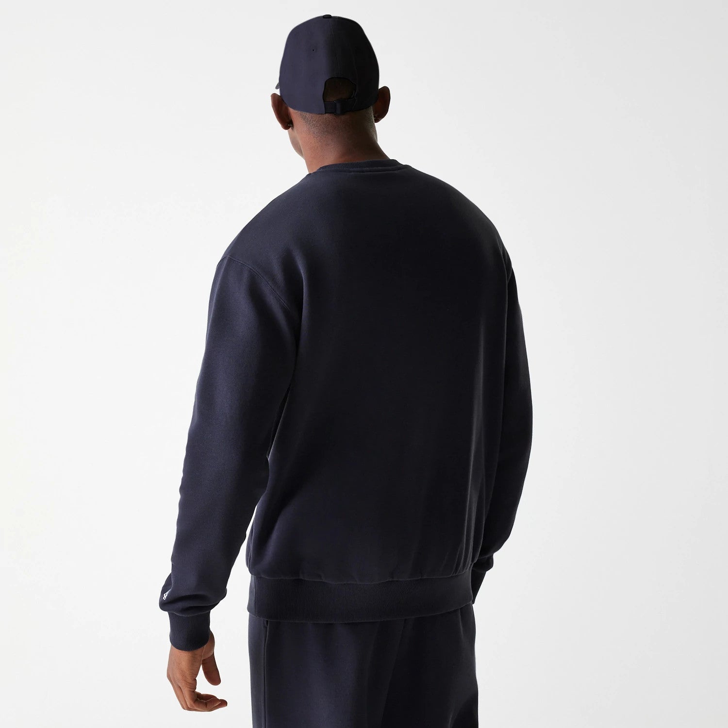 New Era New York Yankees MLB League Essential French Terry Navy Crew Neck Sweater, back view on a model wearing matching navy trousers and a cap, showing the plain navy fabric with a ribbed hem and cuffs.