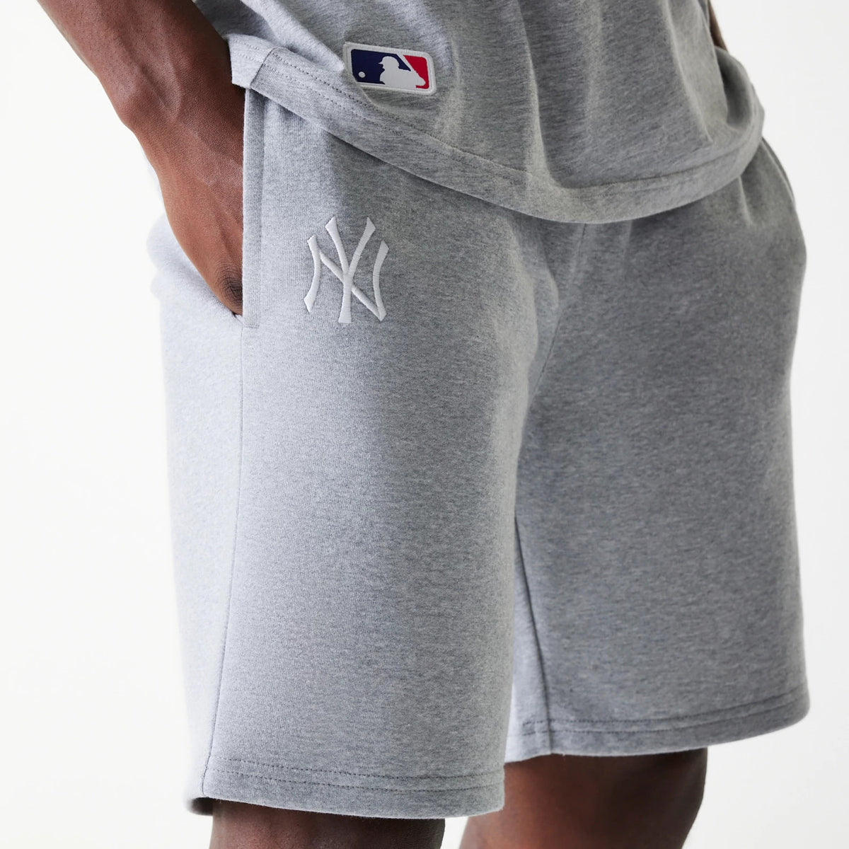 New Era New York Yankees MLB League Essential French Terry Grey Shorts, on-model view showing the soft grey fabric with a raised white New York Yankees logo on the left thigh and a small MLB logo patch on the upper hem of the matching grey top.