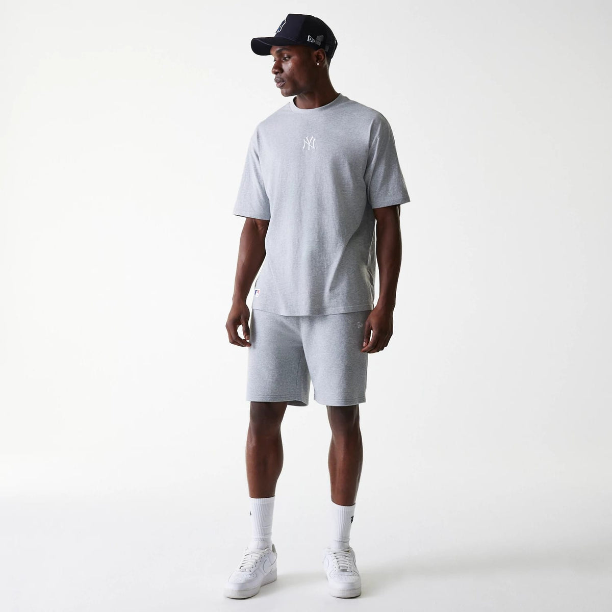 New Era New York Yankees MLB League Essential French Terry Grey Shorts, on-model view showing soft grey colour shorts paired with a matching grey T-shirt, both featuring the New York Yankees logo, styled with white trainers and a black cap.
