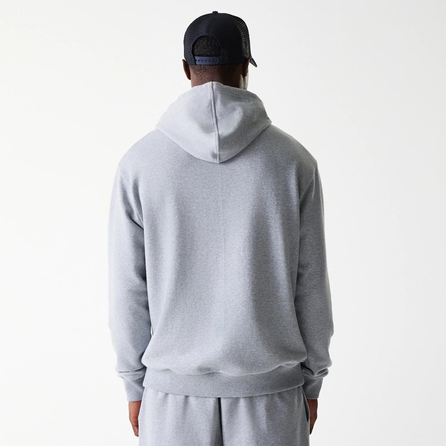 New Era New York Yankees MLB League Essential Midi French Terry Grey Oversized Pullover Hoodie, rear view showing the plain grey back with a relaxed hood, long sleeves, and ribbed hem, worn by a person in matching grey trousers.