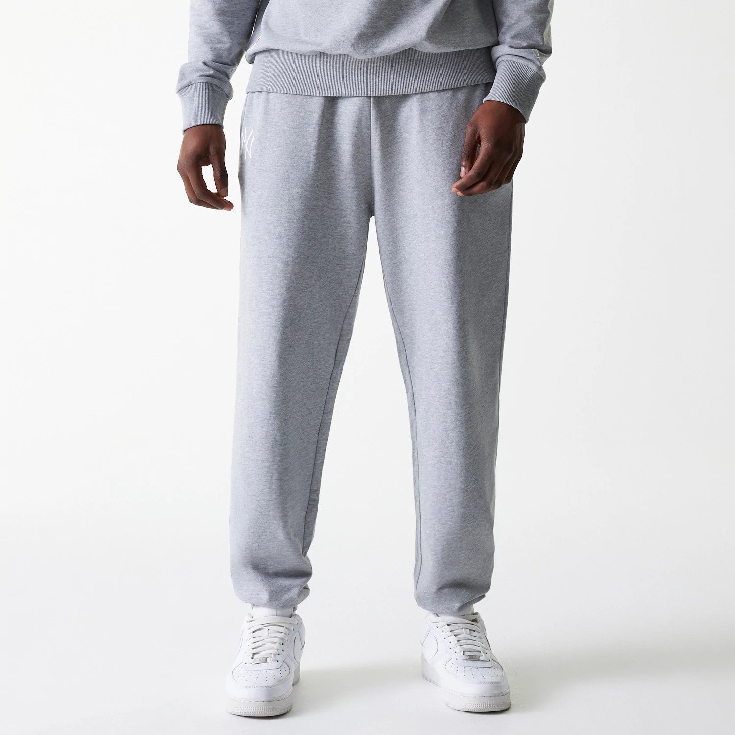 New Era New York Yankees MLB League Essential Midi French Terry Grey Joggers, front view on a model wearing white trainers, featuring the white embroidered NY logo on the left thigh and ribbed waistband.