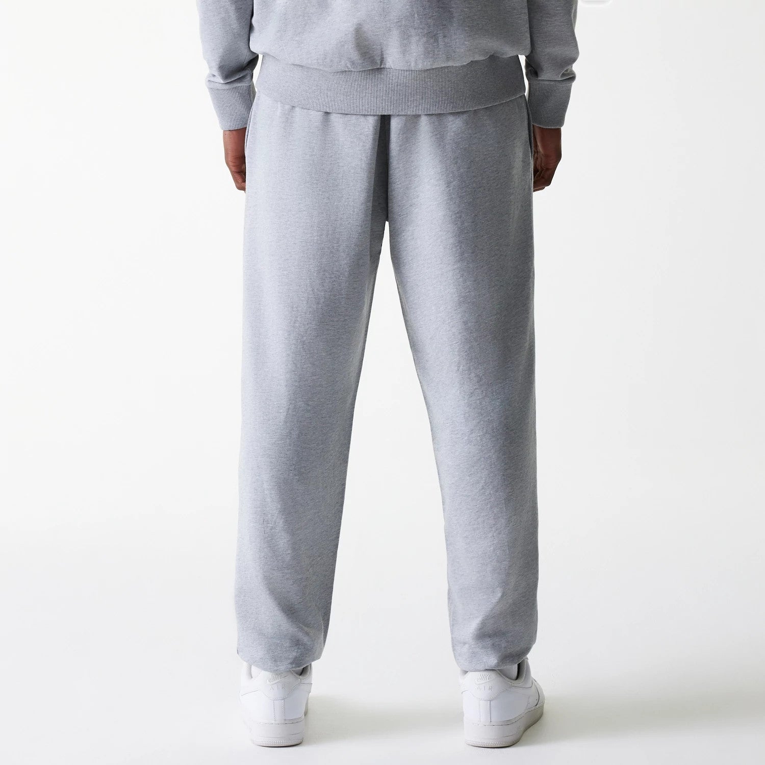 New Era New York Yankees MLB League Essential Midi French Terry Grey Joggers, rear view on a model wearing matching grey sweatshirt, showcasing the relaxed fit and ribbed waistband above plain straight-leg hems with white trainers.