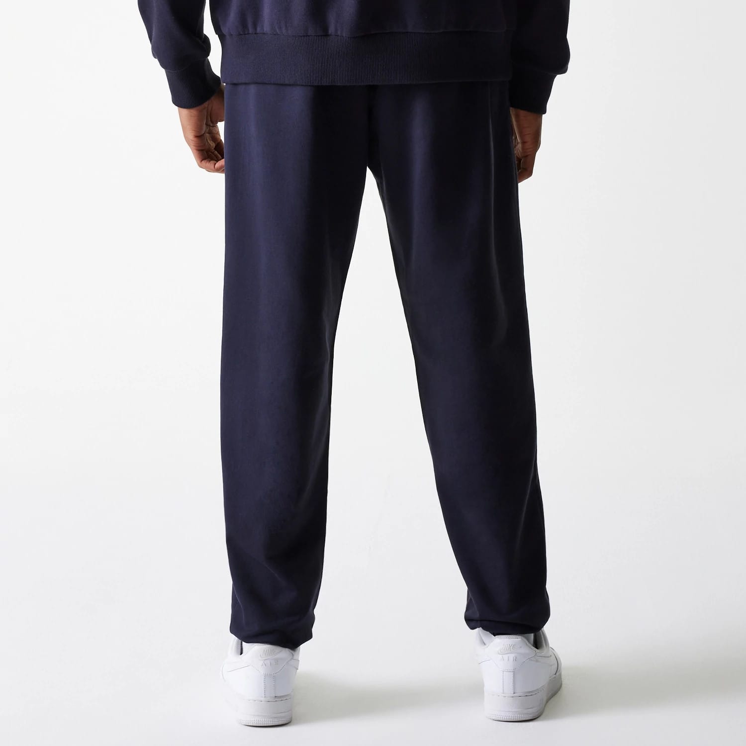 New Era New York Yankees MLB League Essential Midi French Terry Navy Joggers, back view on a model dressed in a matching navy sweatshirt and white trainers, showing the relaxed fit and elasticated waistband.