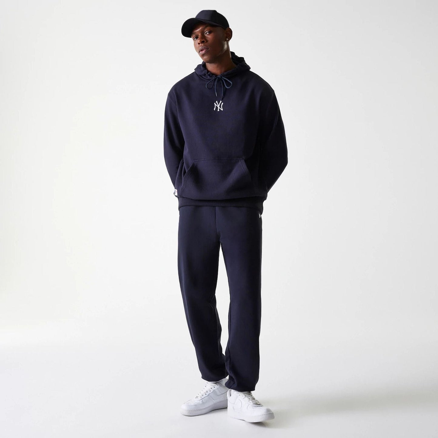 New Era New York Yankees MLB League Essential Midi French Terry Navy Joggers, on a model styled with a navy hooded sweatshirt and cap, showcasing the relaxed fit and ankle cuffs for a sporty casual look.