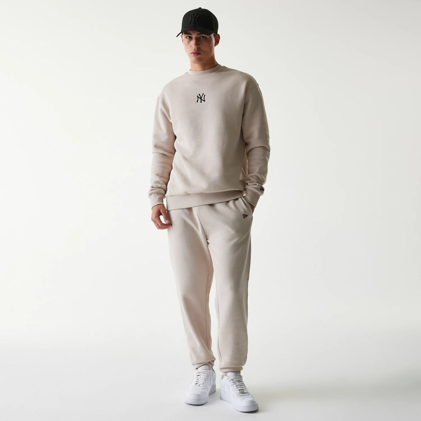New Era New York Yankees MLB League Essential Cream Joggers, on a model styled with a cream sweatshirt and white sneakers, showing a small embroidered New Era flag logo near the left pocket and a relaxed fit.