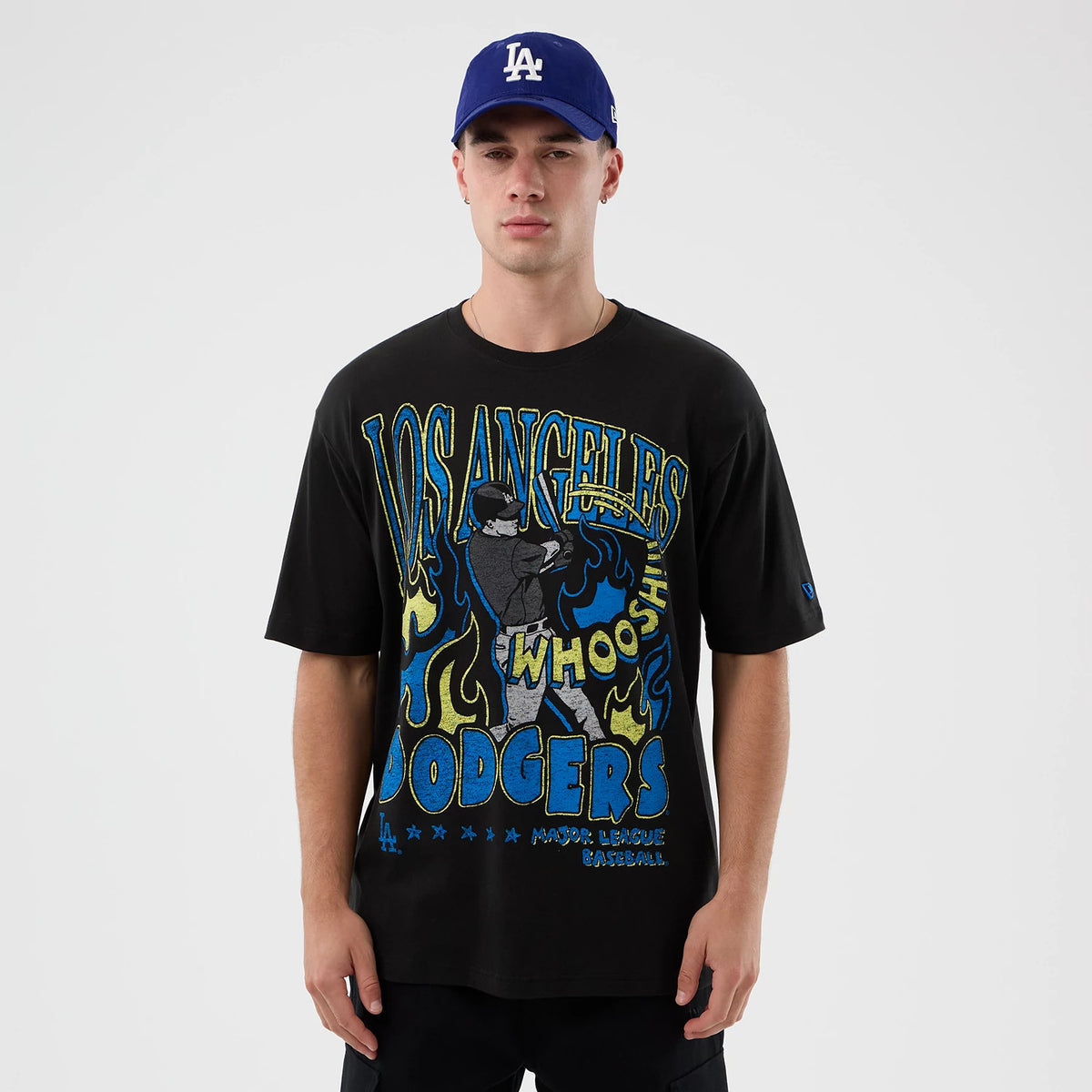 New Era LA Dodgers MLB Player Life Graphic Black T-Shirt, on-model view showing the graphic front design featuring a baseball player with flames, large blue and yellow text, and a debossed New Era logo on the cap worn by the model.