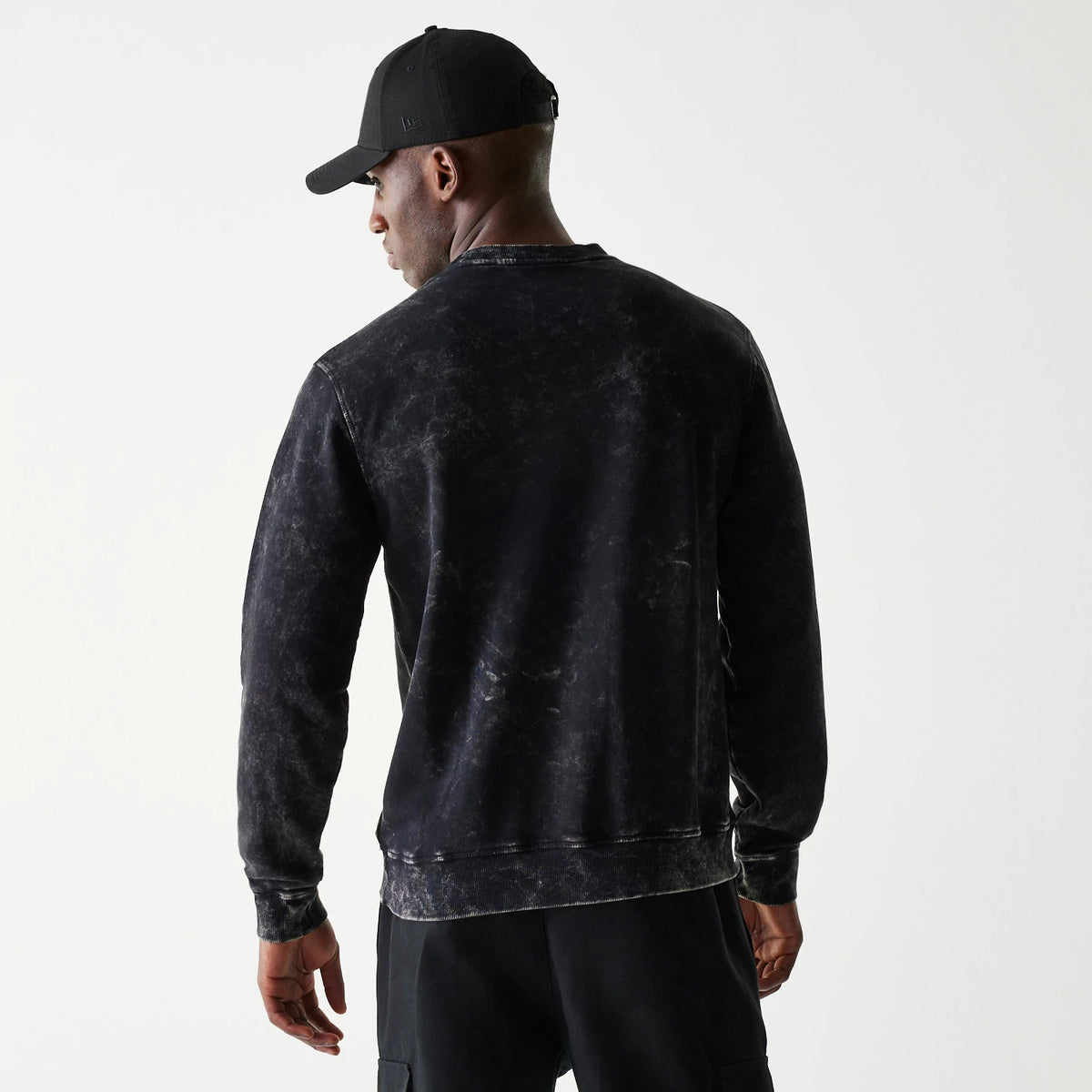 New Era Las Vegas Raiders NFL Throwback Black Crew Neck Sweater, back view on a model wearing a matching black cap, showing the sweater's washed effect and ribbed cuffs with a relaxed fit.