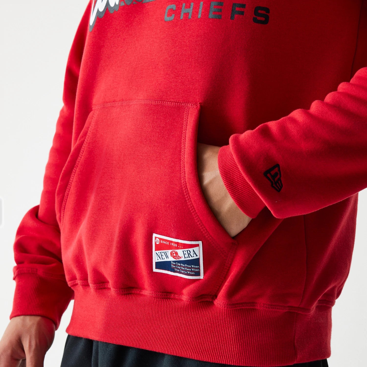 New Era Kansas City Chiefs NFL Throwback Red Pullover Hoodie, side view showing the red fabric with a front pocket, a small New Era logo embossed on the sleeve, a team name across the chest, and a New Era patch above the hem.