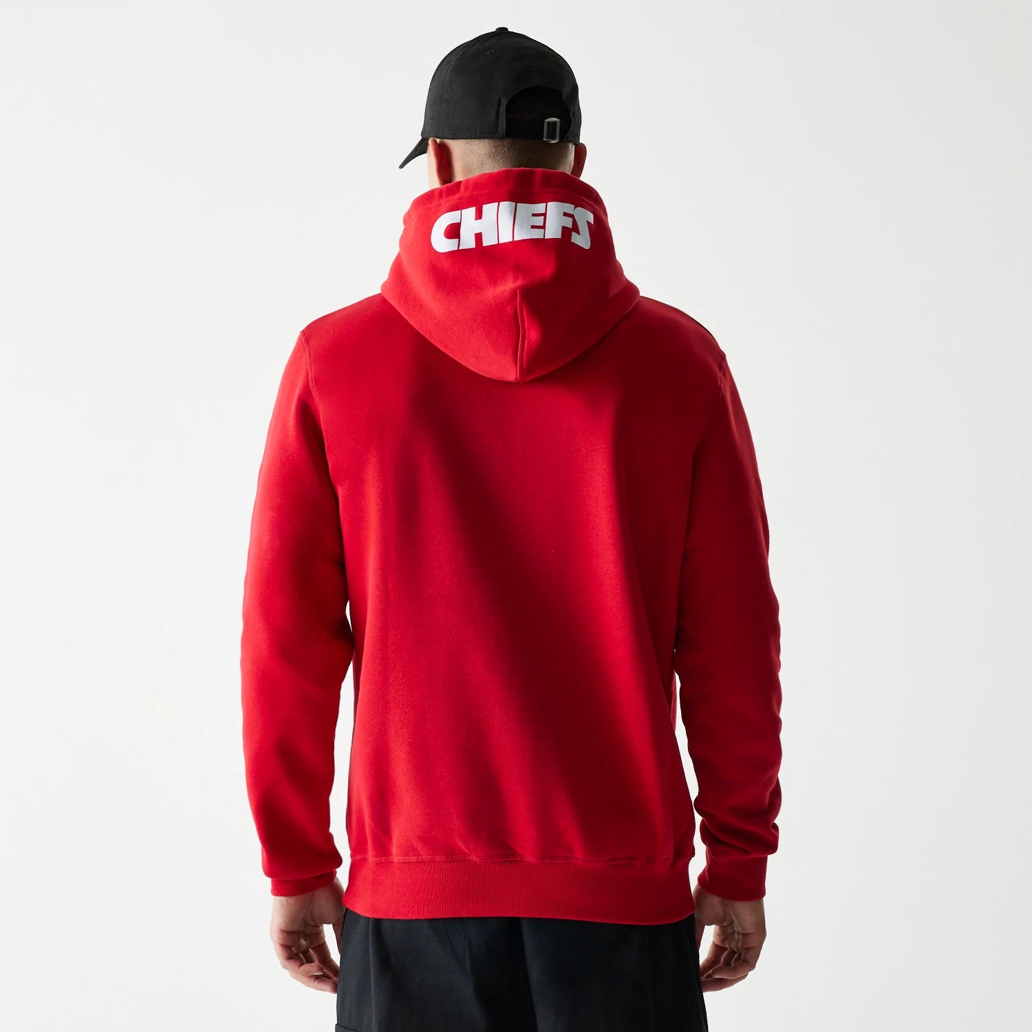 New Era Kansas City Chiefs NFL Throwback Red Pullover Hoodie, rear view showing the bold white CHIEFS lettering across the raised red hood, the solid red back of the pullover, and a person wearing a black cap facing away.