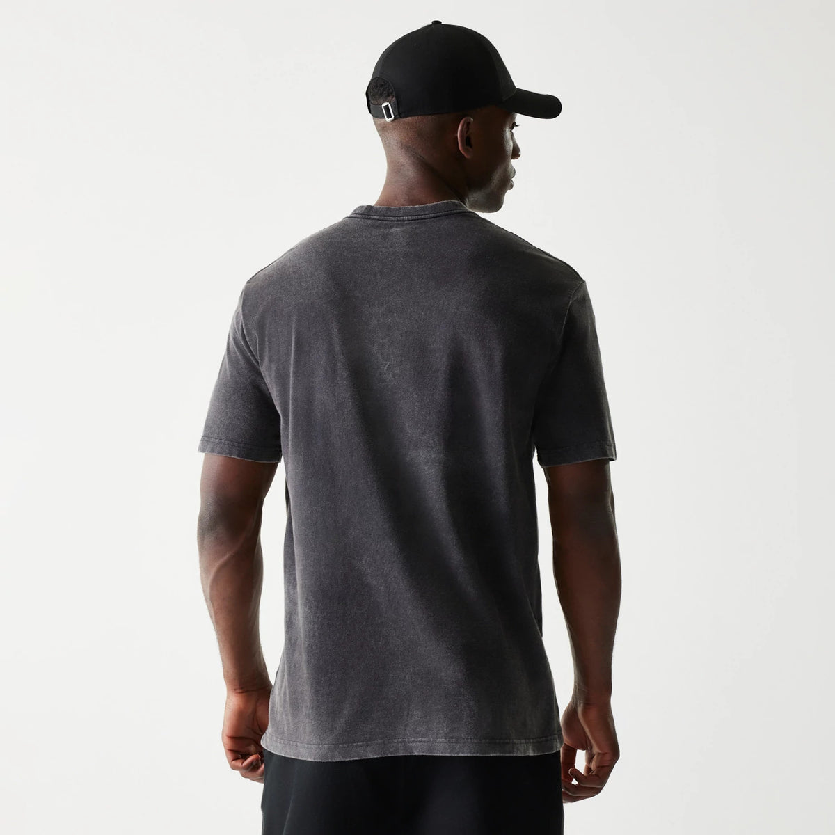 New Era Las Vegas Raiders NFL Sport Night Black T-Shirt, on-model rear view showing the faded black short-sleeve T-shirt with a plain back design, paired with a black cap featuring an embossed logo on the rear above a silver buckle strap.