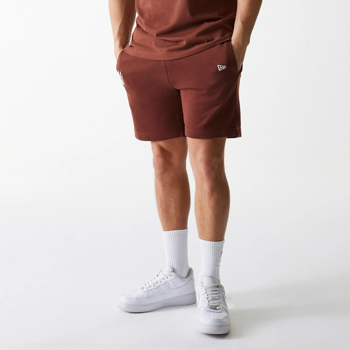 New Era New York Yankees MLB Midi League Essential Brown Shorts, on-model view showing the rich brown colour with a raised New Era logo on the left thigh near the pocket, styled with a matching brown top and white trainers.
