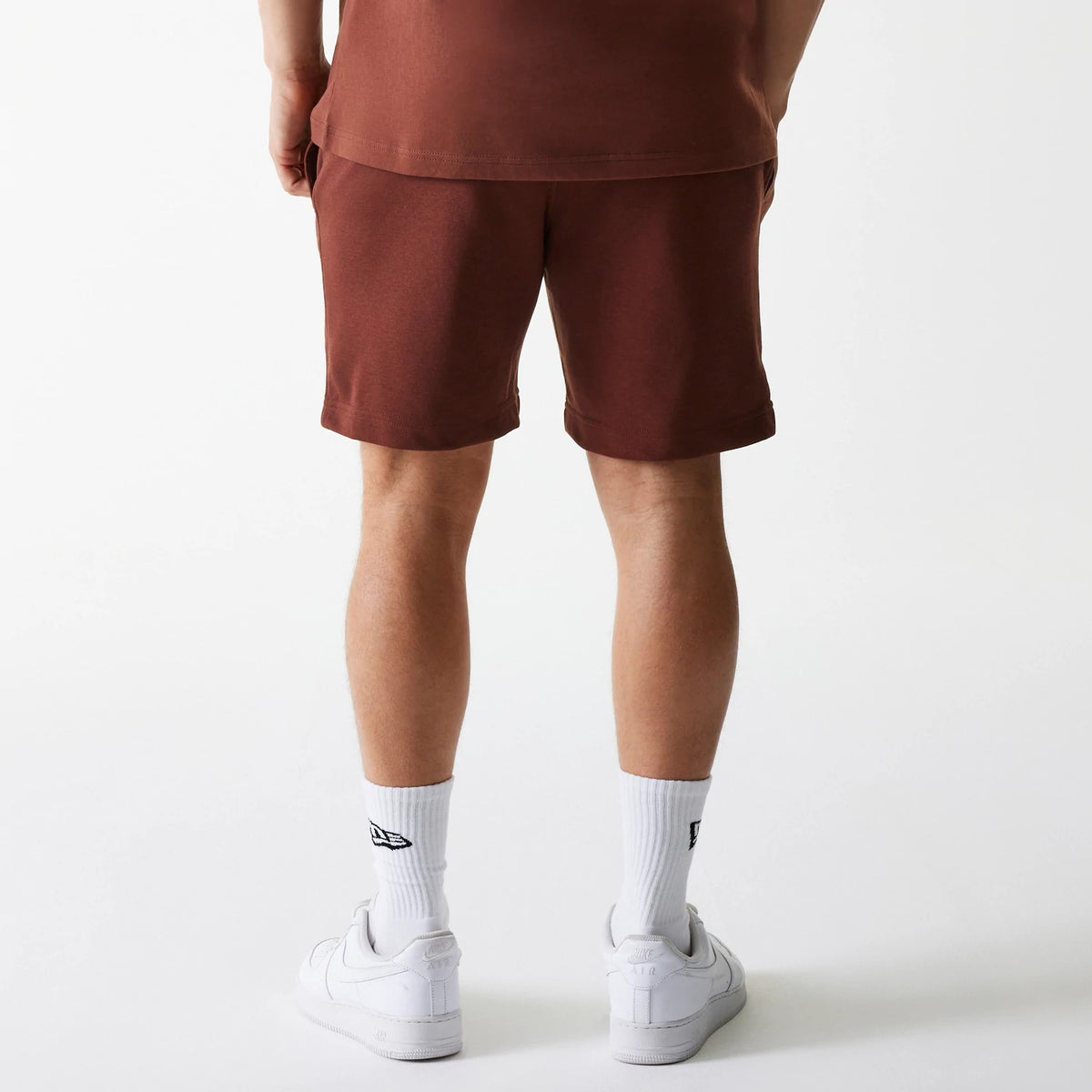 New Era New York Yankees MLB Midi League Essential Brown Shorts, rear view showing the plain brown texture with a straight hem above the knee, worn by a person standing, paired with white socks and sneakers.