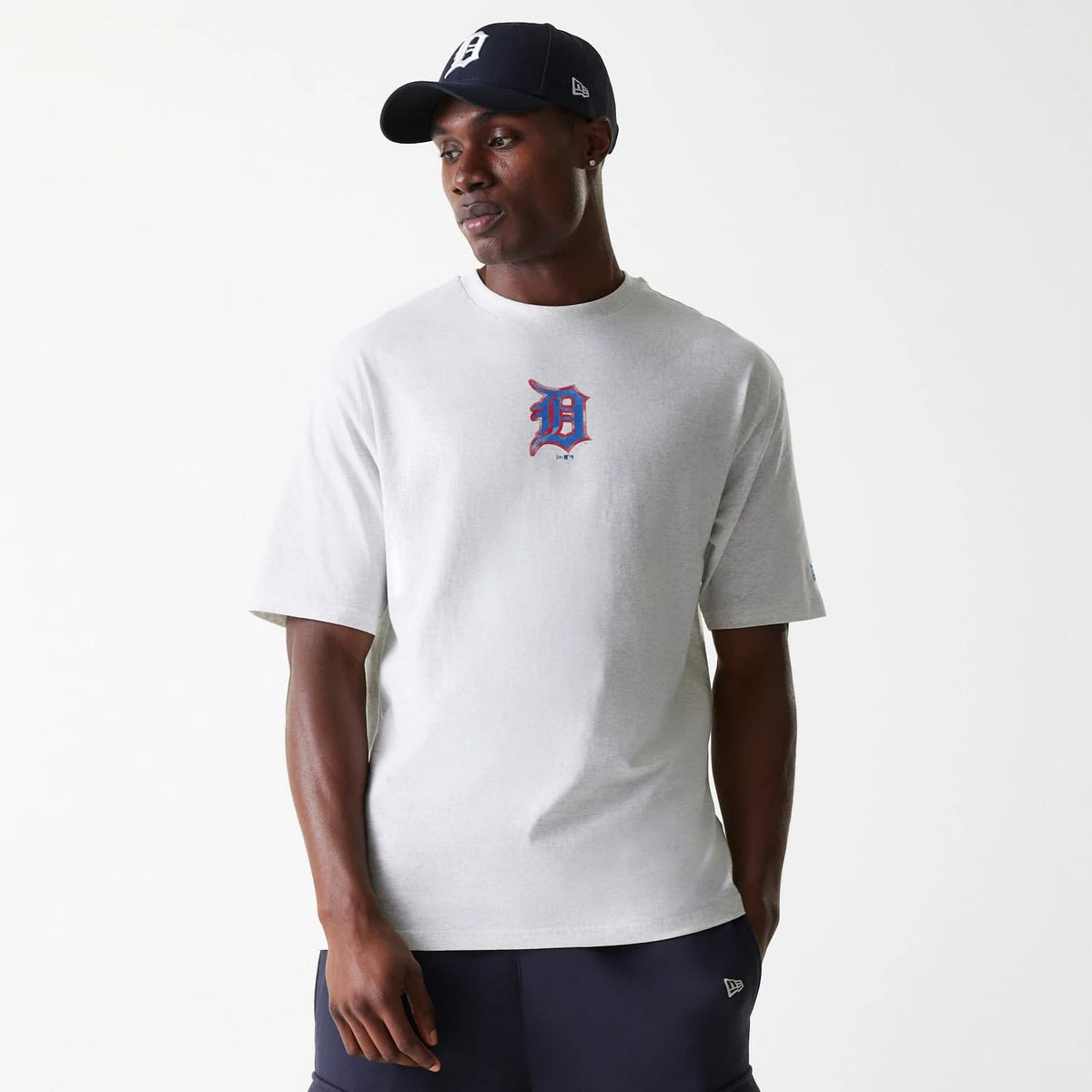 New Era Detroit Tigers MLB World Series Pastel Grey Oversized T-Shirt, on-model view showing the grey shirt with a large blue and orange Detroit Tigers logo on the chest, short sleeves and a relaxed fit, paired with a navy cap.