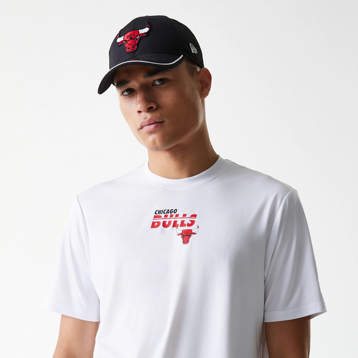 New Era Chicago Bulls NBA Essentials White T-Shirt, on-model view showing the red and black Chicago Bulls logo and text centred on the chest, paired with a black cap featuring a raised red Chicago Bulls logo on the front.