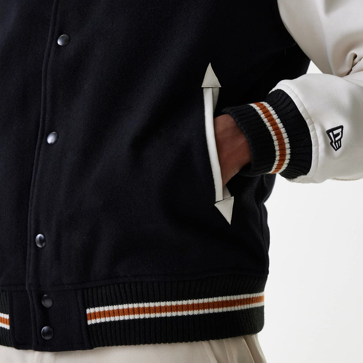 New Era New York Yankees MLB Wordmark Black Varsity Jacket, side view highlighting a debossed New Era logo on the left cream sleeve, black snap buttons along the front, black body with striped ribbed hem and cuffs, and white-trimmed pockets.