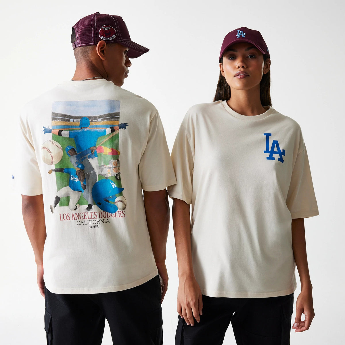 New Era LA Dodgers MLB Baseball Graphic Light Beige Oversized T-Shirt, front and back view showing the blue LA logo on the chest, a large baseball graphic on the back, both worn by models with maroon caps.