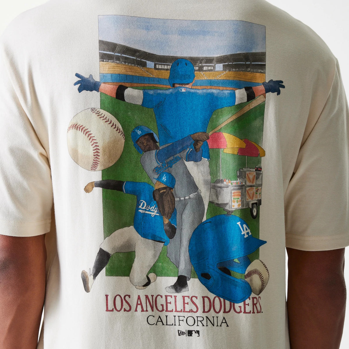 New Era LA Dodgers MLB Baseball Graphic Light Beige Oversized T-Shirt, rear view showing a colourful graphic of players in action with a baseball, bat, and LA cap, set against a stadium backdrop with Los Angeles Dodgers California printed below.