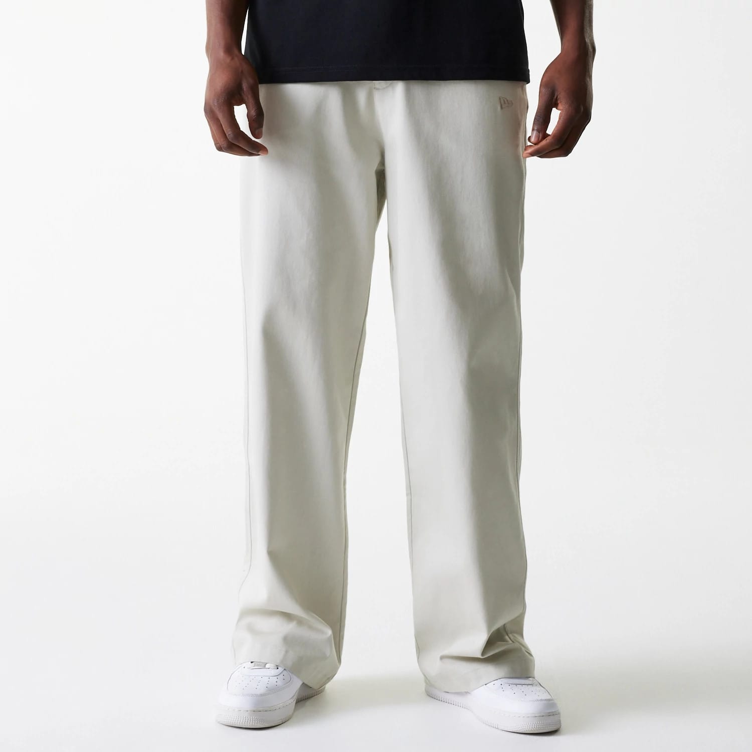 New Era New York Yankees MLB Light Beige Chino Trousers, front view on a model wearing a black top and white sneakers, showing the relaxed fit and the New Era flag logo embroidered on the left pocket area.