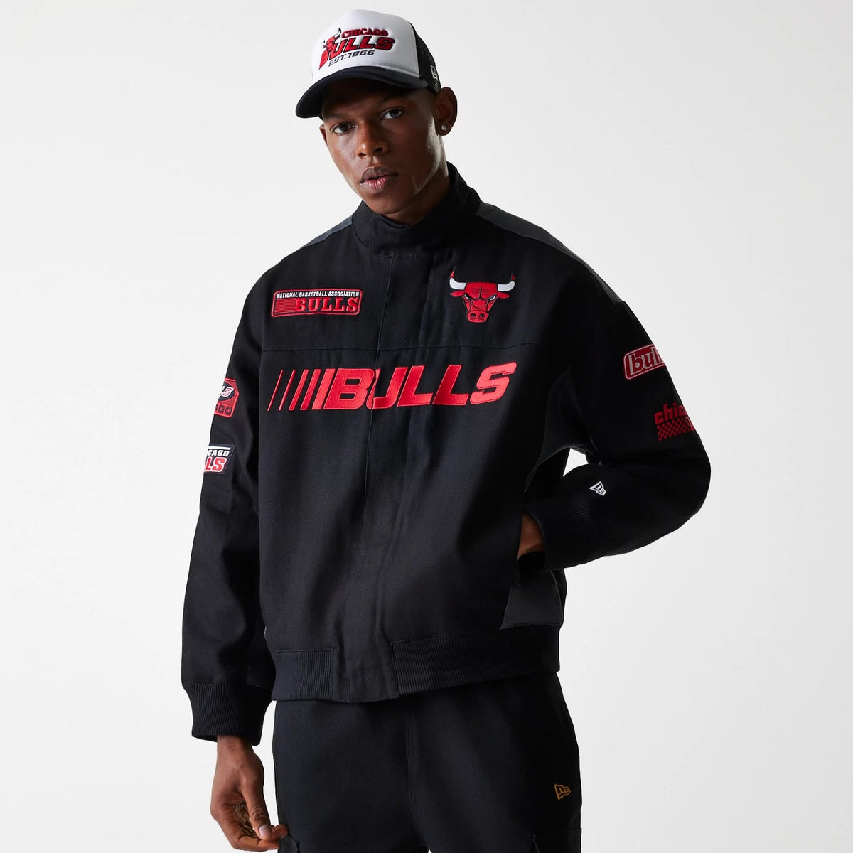 New Era Chicago Bulls NBA Black Motorsports Jacket, front view showing the black jacket with red BULLS lettering across the chest, a red and white embroidered bull logo on the left chest, and various patches on the sleeves.