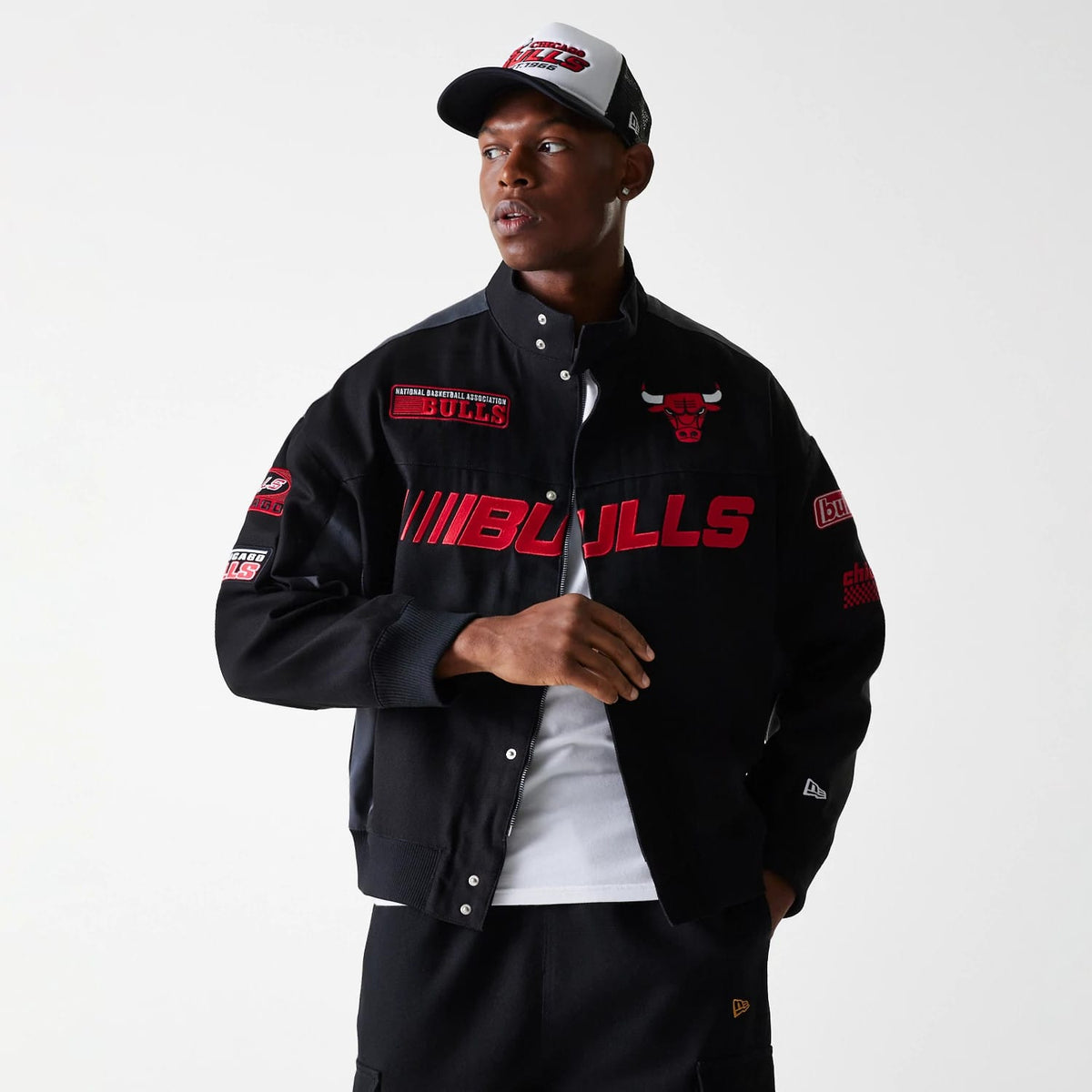 New Era Chicago Bulls NBA Black Motorsports Jacket, on-model view showing a black jacket with red Bulls graphics across the front, a debossed New Era logo on the left cuff, various patches on the sleeves and collar, and a red Bulls logo on the chest.