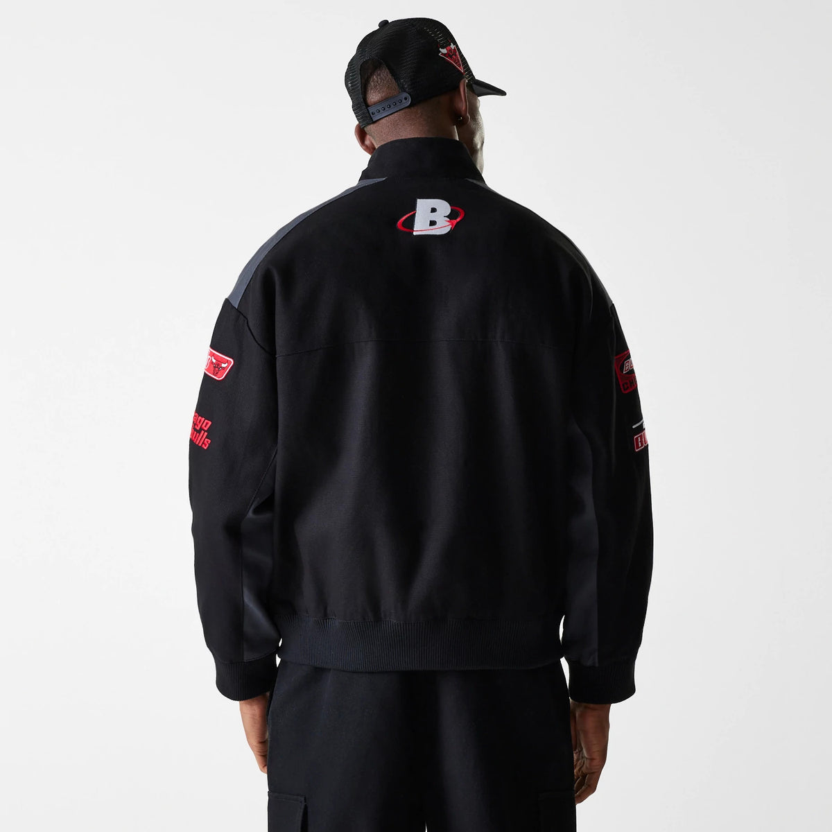 New Era Chicago Bulls NBA Black Motorsports Jacket, rear view featuring the large embroidered 'B' logo centred on the upper back, red and white accents on the sleeves, and a relaxed black fit worn by a model with a black cap.
