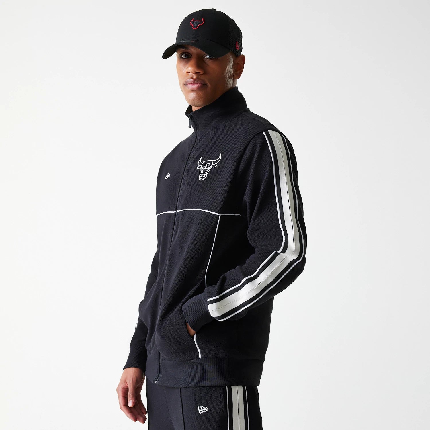 New Era Chicago Bulls NBA Outline Black Track Jacket, on-model view showing a black zip-up jacket with white piping and stripes along the sleeves, a debossed Chicago Bulls logo on the chest and a New Era logo on the left side.