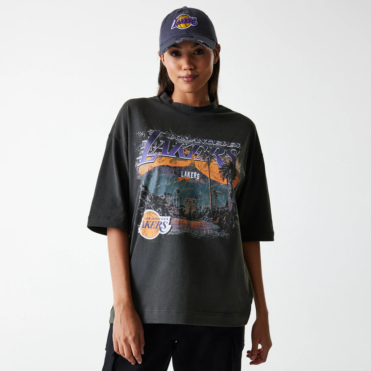 New Era LA Lakers NBA Washed Graphic Grey T-Shirt, on-model view showing a dark grey T-shirt with a large Lakers graphic printed across the chest and a New Era logo on a grey cap worn by the model.