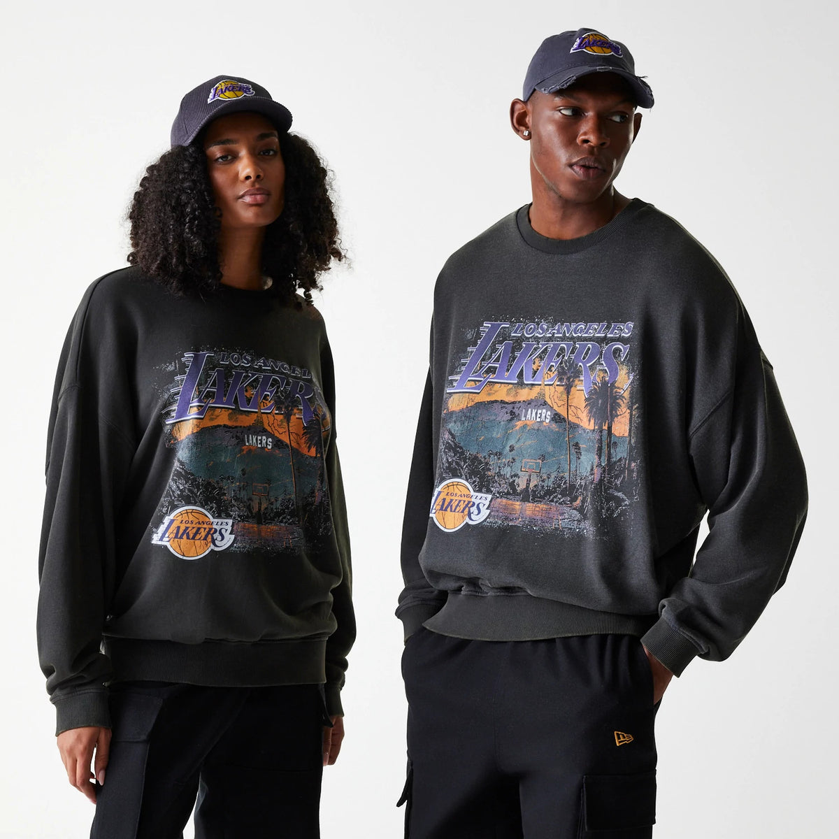 New Era LA Lakers NBA Washed Graphic Grey Oversized Crew Neck Sweater, front view on models pairing the jumper with matching grey caps featuring the Lakers logo, highlighting the vintage graphic print across the chest.