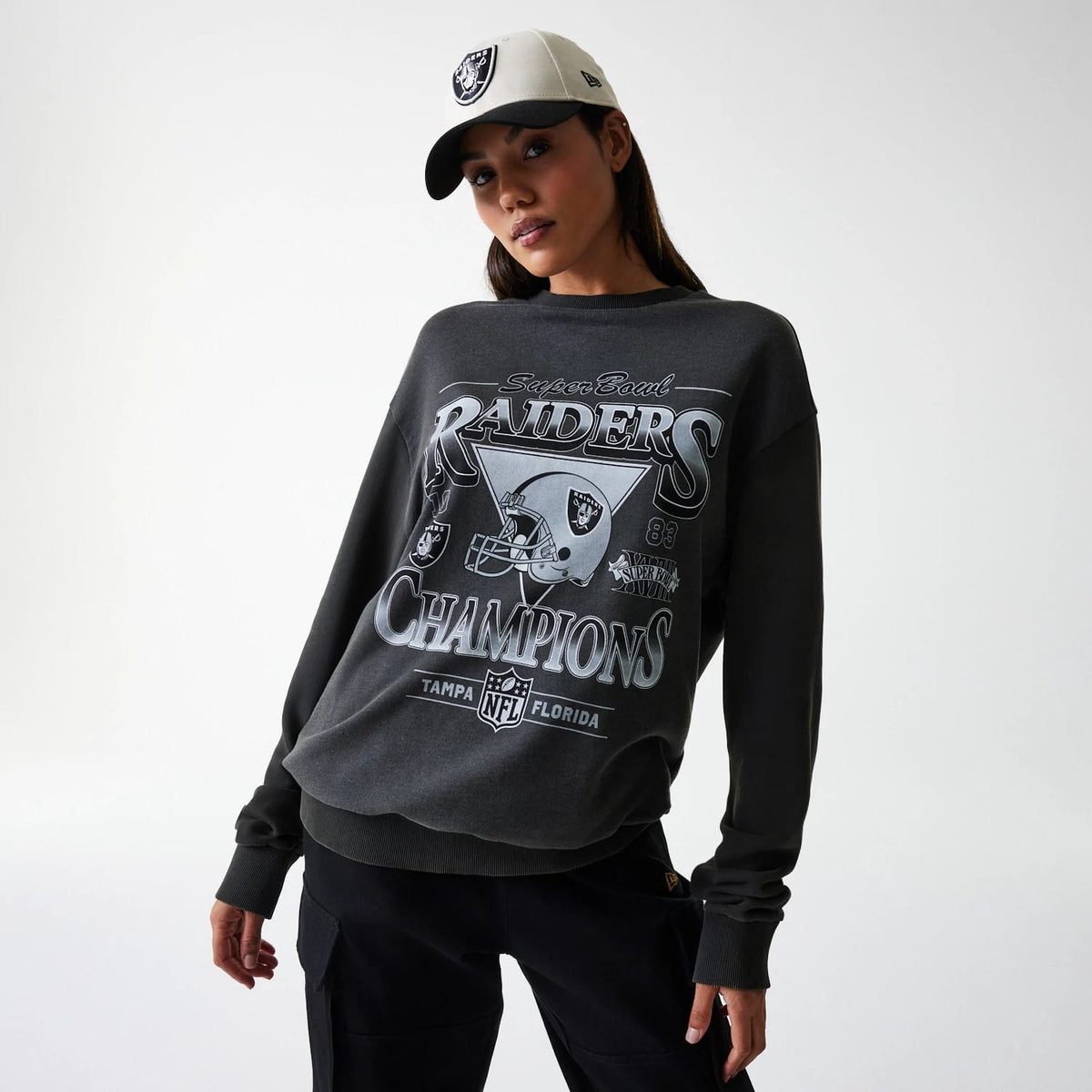 New Era Las Vegas Raiders NFL Washed Super Bowl Grey Oversized Crew Neck Sweater, front view on a model wearing a matching cap, featuring a large Raiders Champions graphic with a helmet and NFL logo across the chest.
