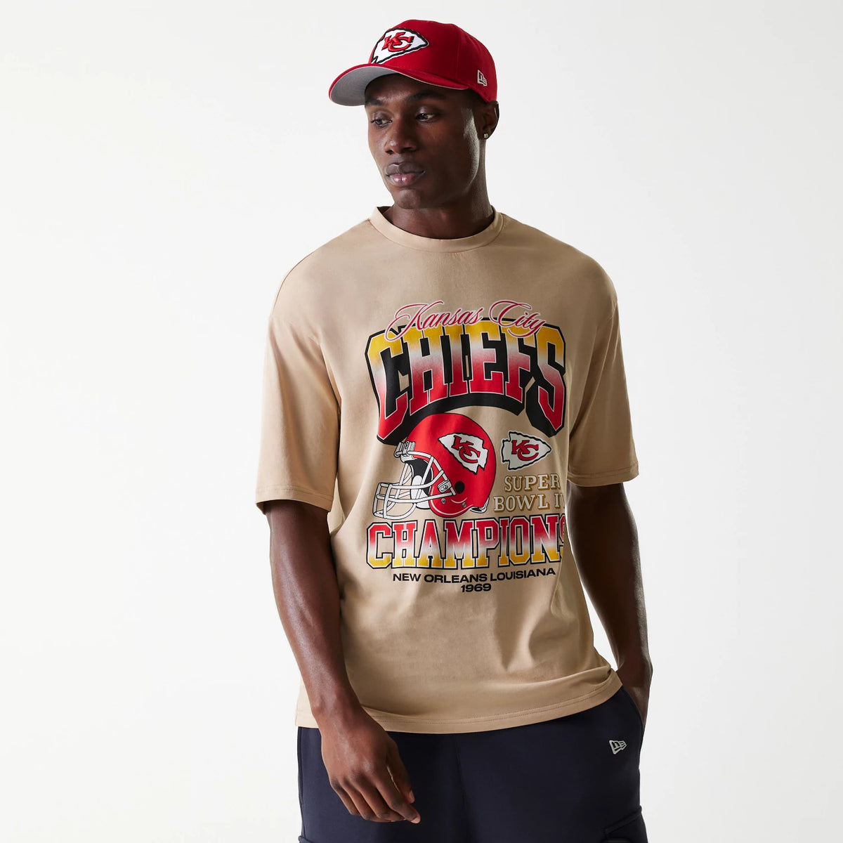 New Era Kansas City Chiefs NFL Washed Super Bowl Beige Oversized T-Shirt, on-model view showing the large front graphic with Kansas City Chiefs text and logos in red, a red helmet design, paired with a red cap featuring an embroidered logo.