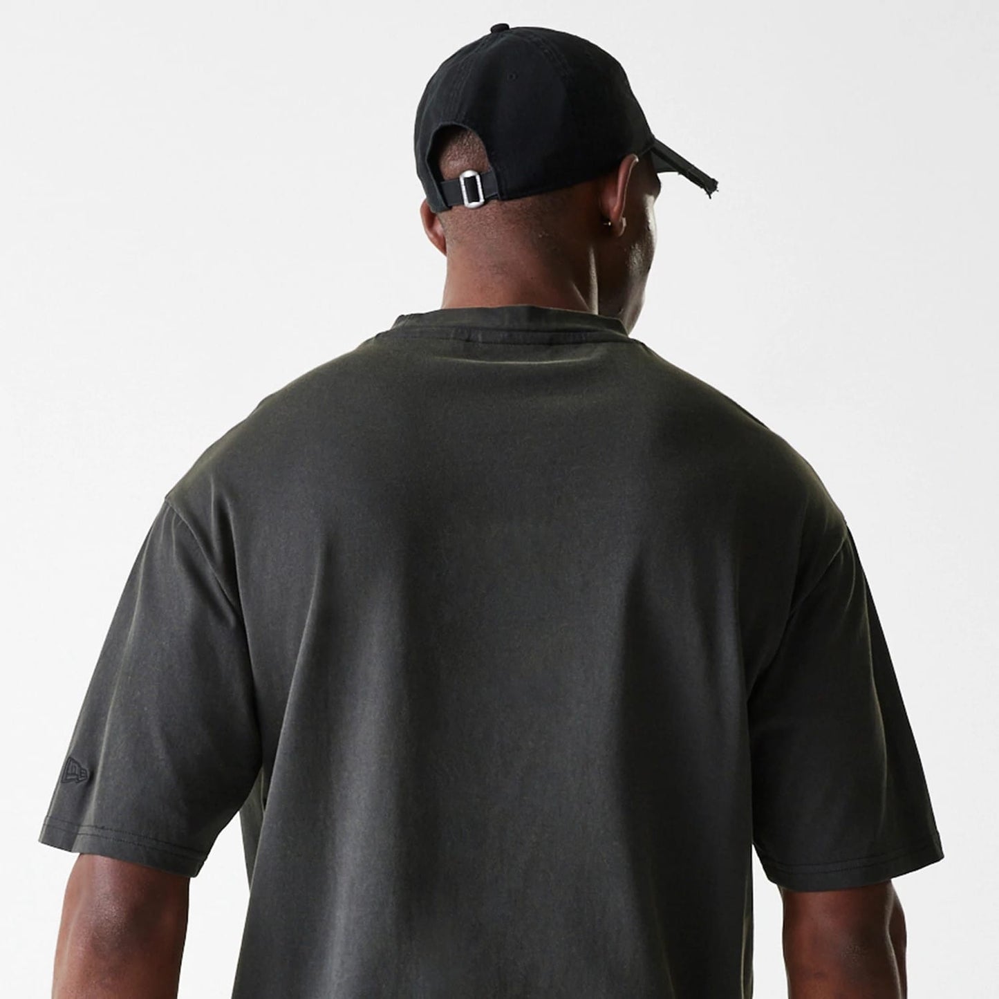New Era Las Vegas Raiders NFL Washed Super Bowl Grey Oversized T-Shirt, rear view showing the washed grey fabric with loose short sleeves, a small debossed logo on the left sleeve, worn by a model in a black cap with a buckle closure.