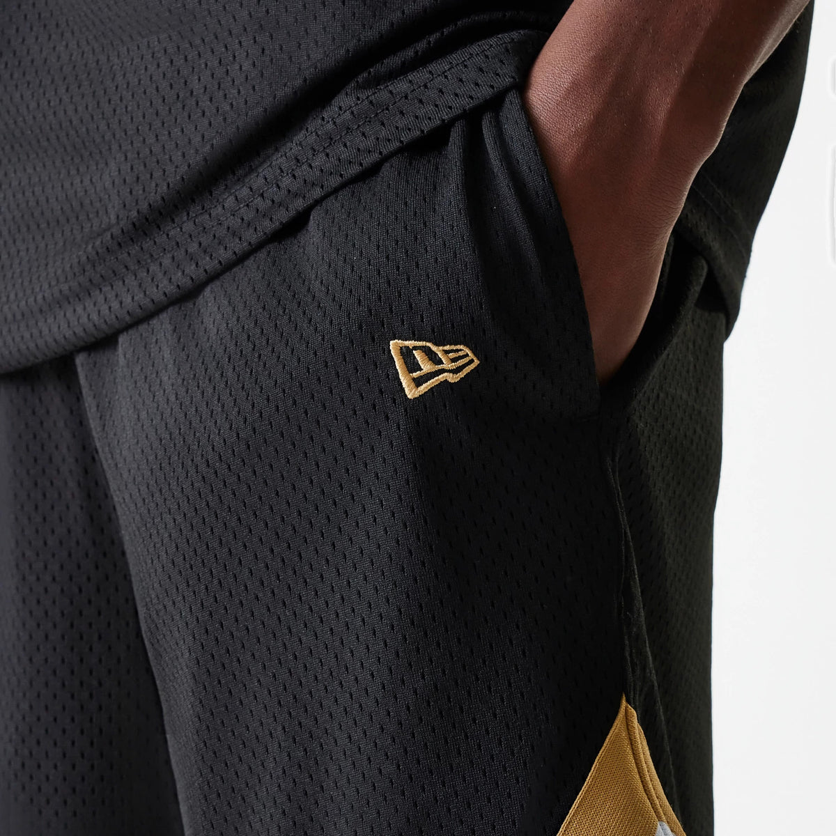 New Era San Francisco 49ers NFL Mesh Black Shorts, side view showing a raised gold New Era logo near the pocket, black mesh fabric texture with a glimpse of an arm casually positioned in the pocket opening.