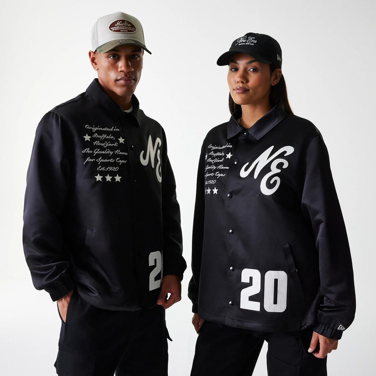 New Era Black Coaches Jacket, on-model view showing two models wearing black jackets with white NE logos on the chest, button-up fronts, script text alongside three stars, and the number 20 in large print near the hem.