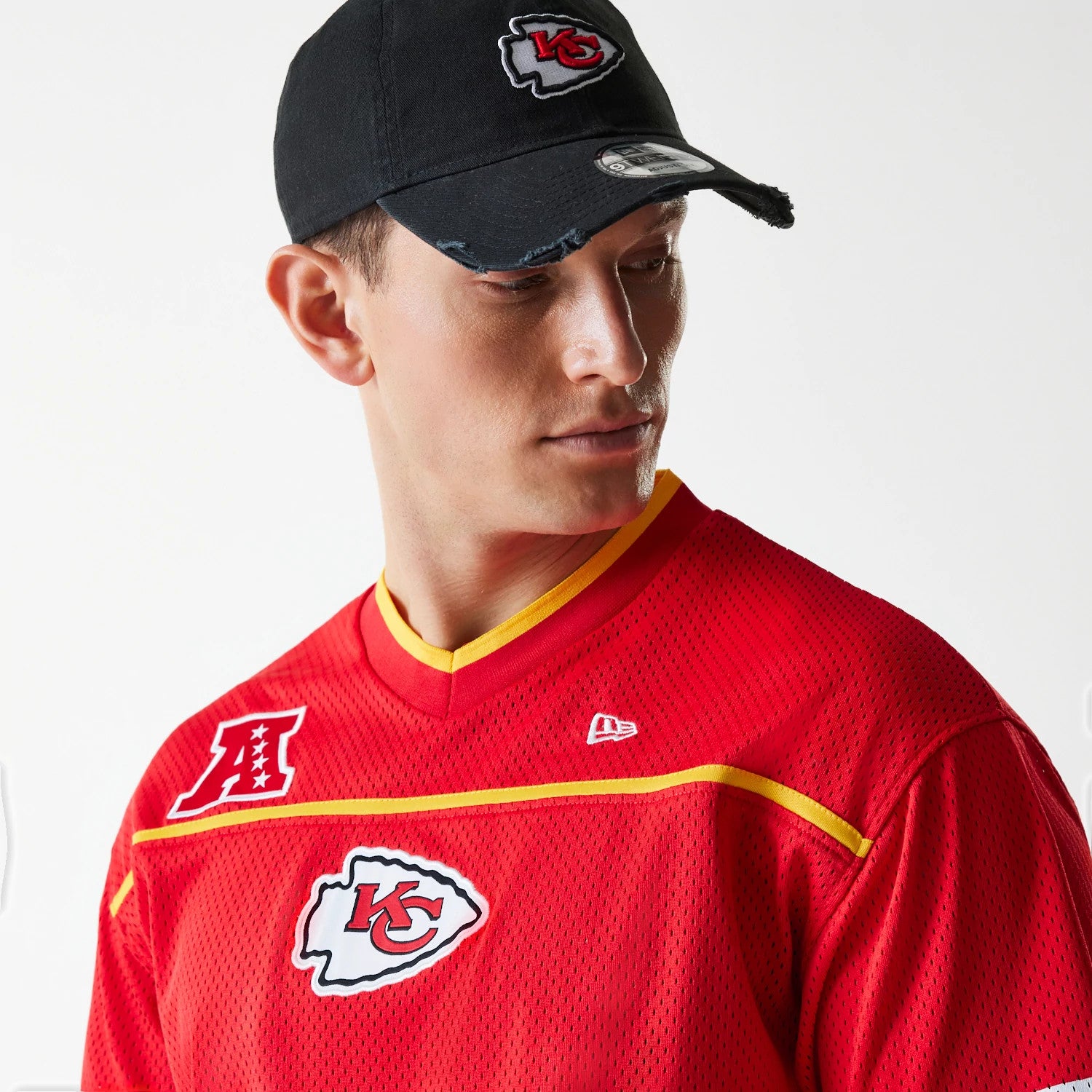 New Era Kansas City Chiefs NFL Mesh Red Jersey, on a model wearing a matching black cap with the Chiefs logo on the front panel, showing red and gold piping at the collar and AFC logo on the upper chest.