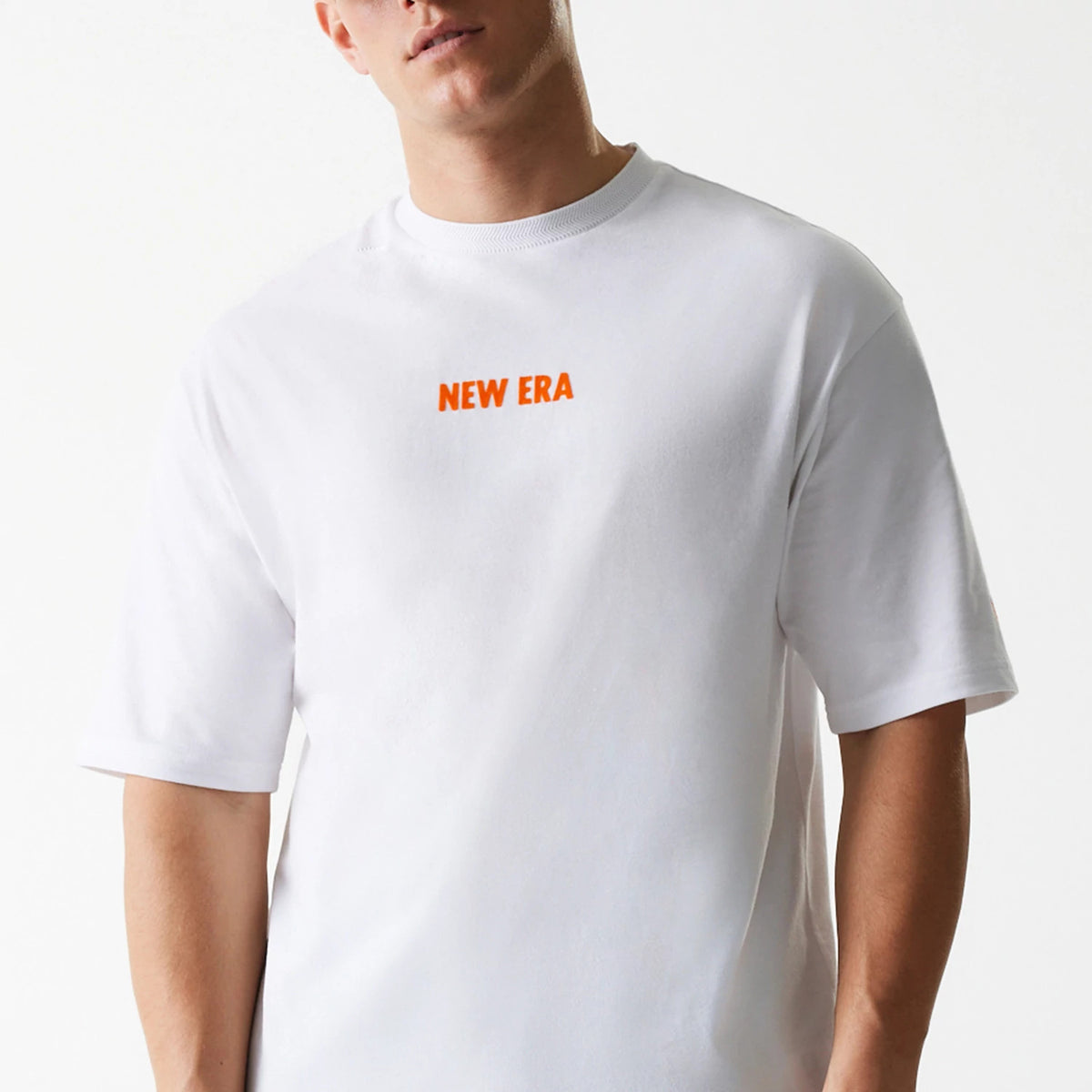 New Era Graphic White Oversized T-Shirt, front view showing a plain white T-shirt with short sleeves and an orange raised New Era logo centred on the chest.