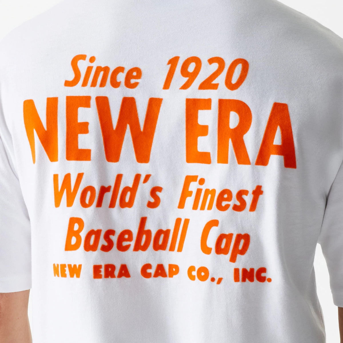 New Era Graphic White Oversized T-Shirt, rear view showing large orange printed text reading Since 1920 NEW ERA World's Finest Baseball Cap on the upper back of the white fabric.
