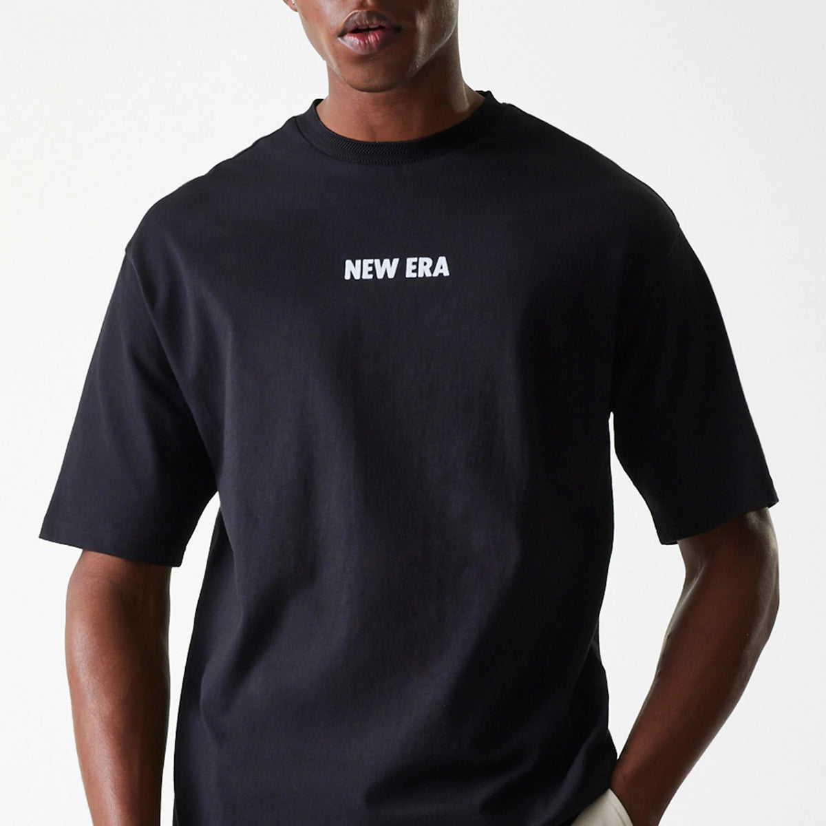 New Era Graphic Black Oversized T-Shirt, front view showing a black T-shirt with a white embossed New Era logo centred on the chest above the relaxed fit torso and sleeves.