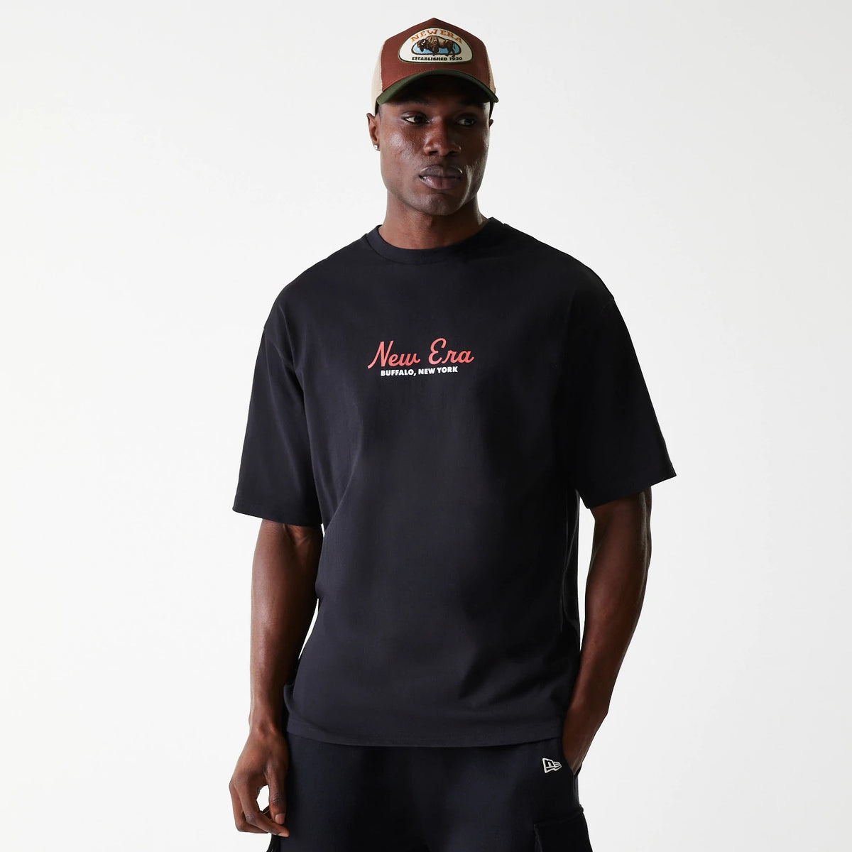 New Era Animal Graphic Black Oversized T-Shirt, on-model view featuring a black oversized t-shirt with a red and white debossed New Era Buffalo, New York logo across the chest, worn by a person in black shorts and a brown and green cap.