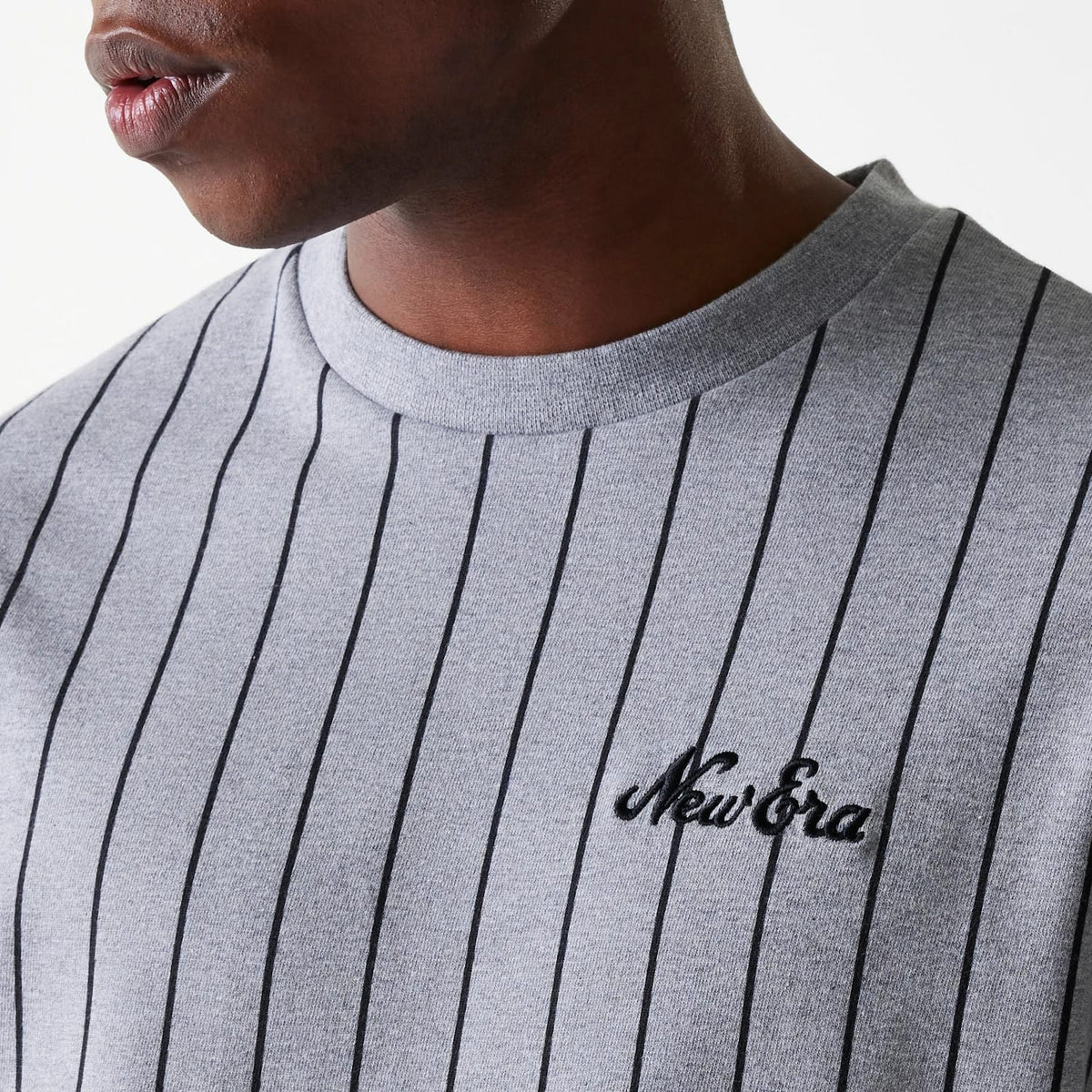 New Era Pinstripe Pastel Grey Oversized T-Shirt, on-model view showing the black embroidered New Era logo on the left chest, classic crew neckline, and vertical black pinstripes on the pastel grey fabric.
