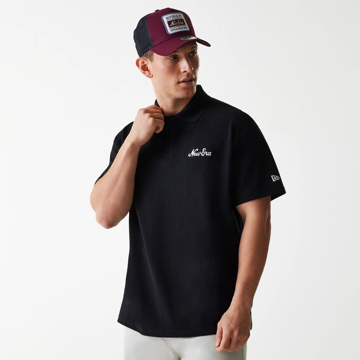New Era Script Black Polo T-Shirt, on-model view featuring a white New Era script logo on the left chest, paired with a purple cap with a raised patch, and an embroidered New Era logo on the left sleeve.