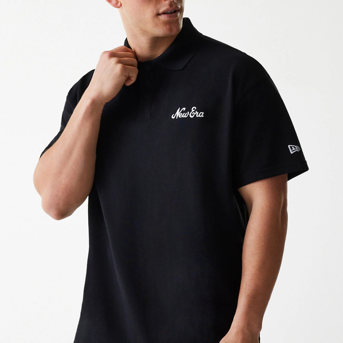 New Era Script Black Polo T-Shirt, on-model view showing the black polo shirt worn by a person, with an embroidered white New Era script logo on the left chest and a small white embroidered logo on the left sleeve.