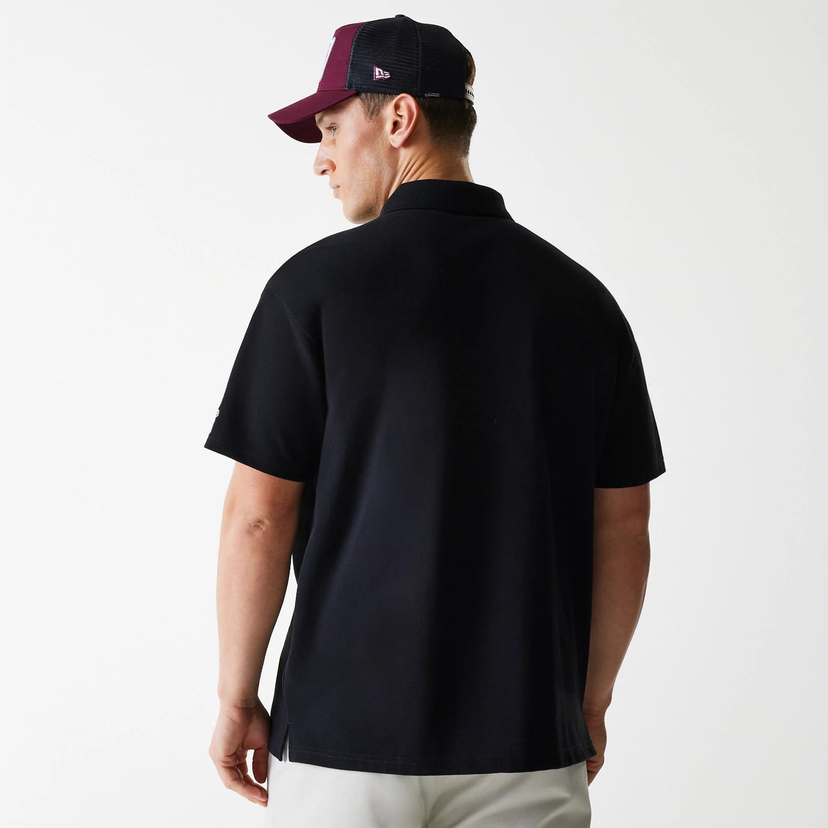 New Era Script Black Polo T-Shirt, on-model rear view showing the plain black back with short sleeves, alongside a maroon and black mesh cap featuring a raised New Era logo on the side.
