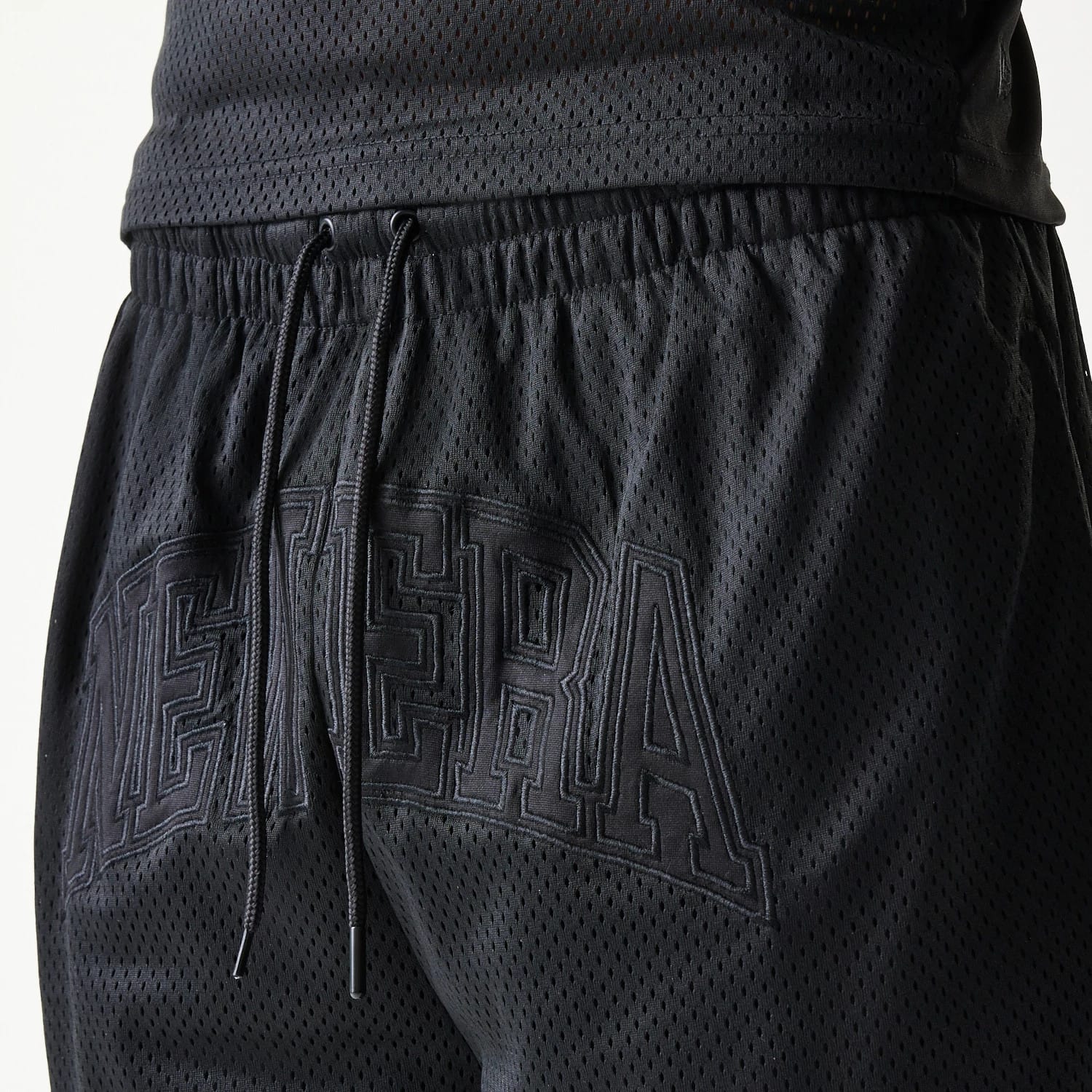 New Era Mesh Black Shorts, side view showing black mesh fabric with an elasticated waistband, drawstrings hanging in front, and a large embossed New Era logo across the back of the shorts.