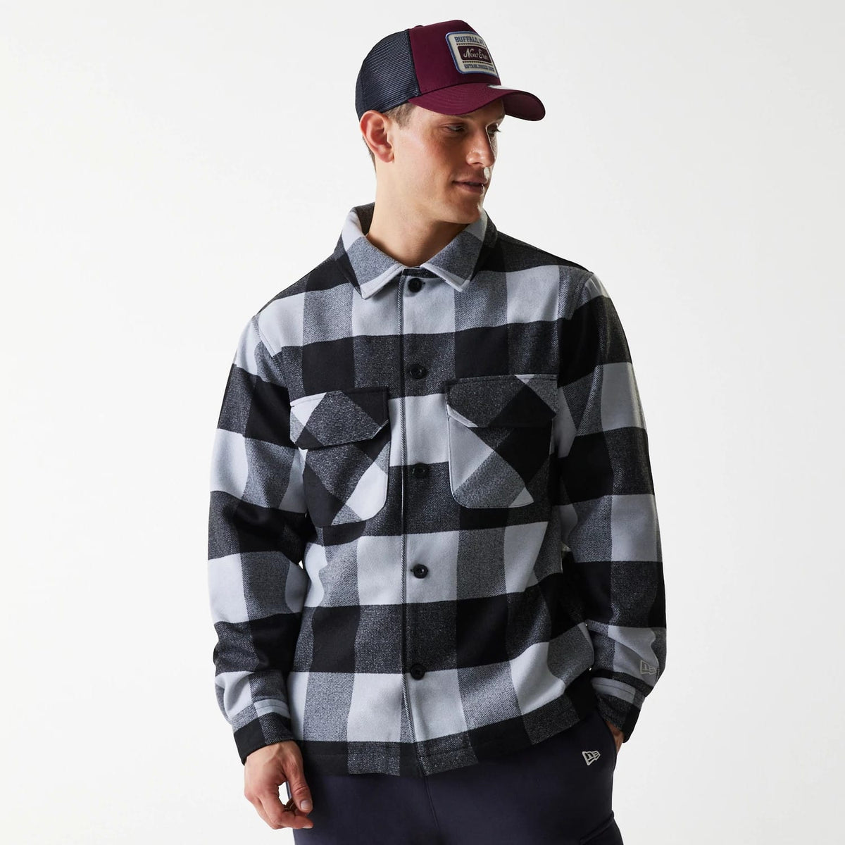 New Era Black Shacket, on-model view with a black and grey checkered pattern, featuring two chest pockets with button closures, styled with a dark coloured cap featuring a front patch.