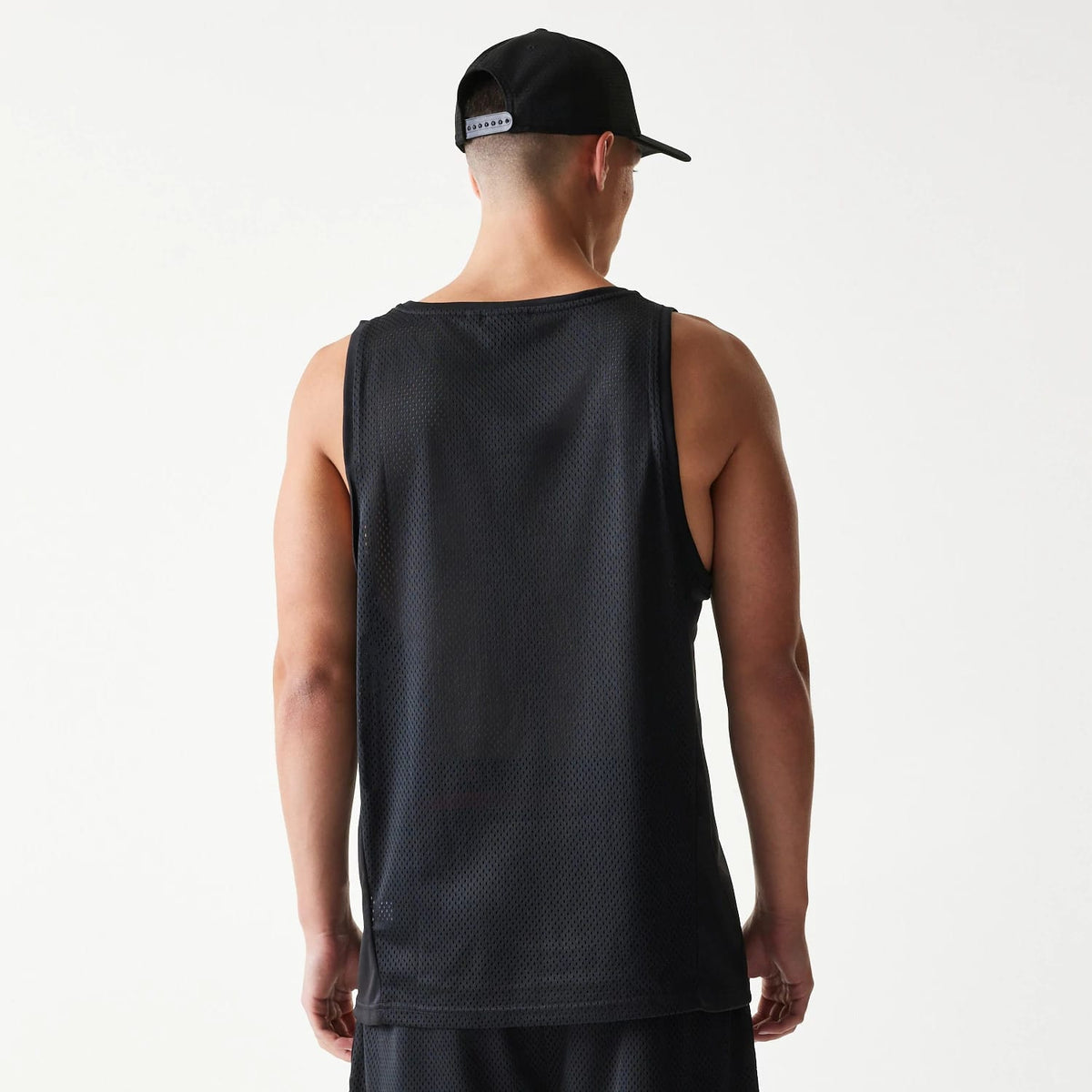 New Era Mesh Black Mesh Vest, back view on a model wearing the vest with matching shorts, showing the sleeveless design and textured mesh fabric, complemented by a black cap with an adjustable snapback closure.