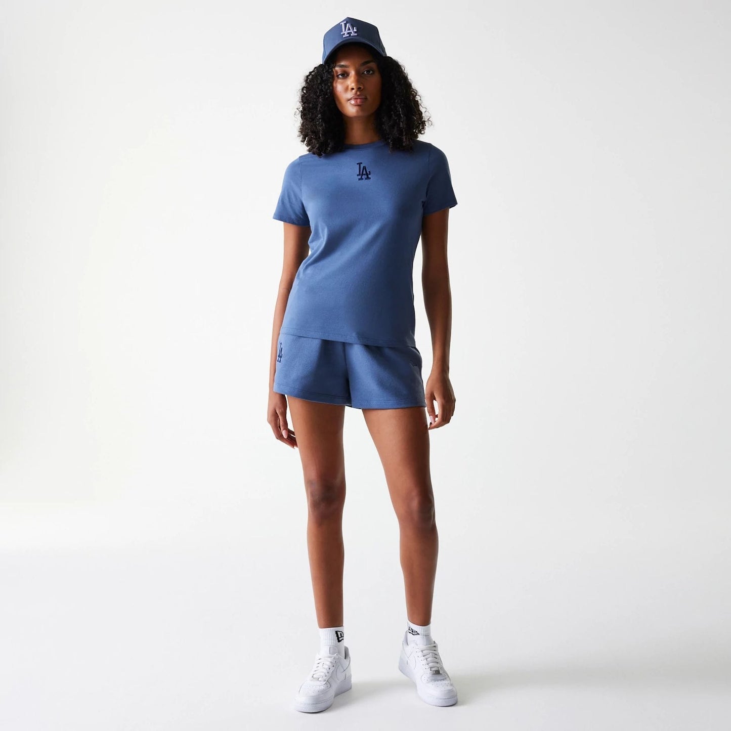New Era LA Dodgers Womens MLB Midi League Essential Dark Blue Shorts, on-model view showing matching dark blue shorts and T-shirt with debossed LA logos, paired with a dark blue cap featuring a raised LA logo on the front.